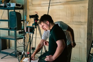 Man adjusting camera equipment on tripod in studio setting with professional lighting